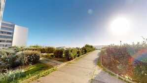 A pathway flanked by dense shrubbery and a building with a white facade. - Air Marin - Apartment Balcony Ocean View (Saint-Hilaire-de-Riez)