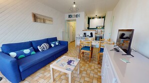 A compact living space with a blue sofa, a small dining table, and a kitchenette area. - Air Marin - Apartment with a Balcony and Ocean View (Saint-Hilaire-de-Riez)