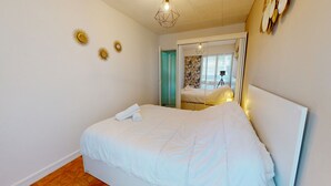 A bedroom with a bed, a door leading to another room, and a ceiling light fixture. - Air Marin - Apartment Balcony Ocean View (Saint-Hilaire-de-Riez)
