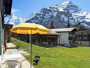 Une terrasse avec des sièges extérieurs, un parasol jaune et une vue sur des montagnes enneigées.
