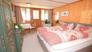 Een slaapkamer met een groot bed, een houten garderobe, een bureau met stoel, en een raam met gordijnen.