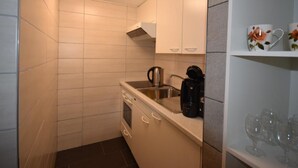 Een compacte keuken met witte kastjes, een inbouwoven, een koffiezetapparaat en een spoelbak.