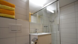Een moderne badkamer met een glazen douchecabine, een wastafel met spiegel en een handdoekrek met gele handdoeken.