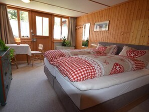 A bedroom with a large bed, wooden walls, a desk, and a chair. - Studio bim Chilchli by Interhome (Lauterbrunnen)