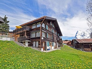 A multi-story wooden chalet with a balcony, situated on a hillside with a view of snow-capped mountains. - Studio bim Chilchli by Interhome (Lauterbrunnen)