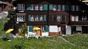 Een houten chalet met balkon, een eethoek met terrasmeubilair en een berg op de achtergrond.