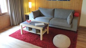 A cozy living room with a grey sofa, a wooden coffee table, and a red rug. - Lengwald "Hiisli" by Interhome (Lauterbrunnen)