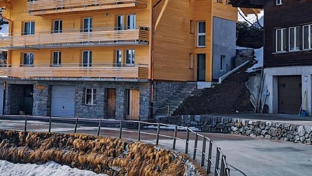 Ein mehrstöckiges Holzgebäude mit Balkonen, einer Steinfassade und einem Blick auf die Berge.