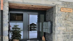 Ein Gebäudehauseingang aus Stein mit Holzbalkendecke, einem Schild mit der Aufschrift 'Raufthubel' und einer kleinen Weihnachtstanne.