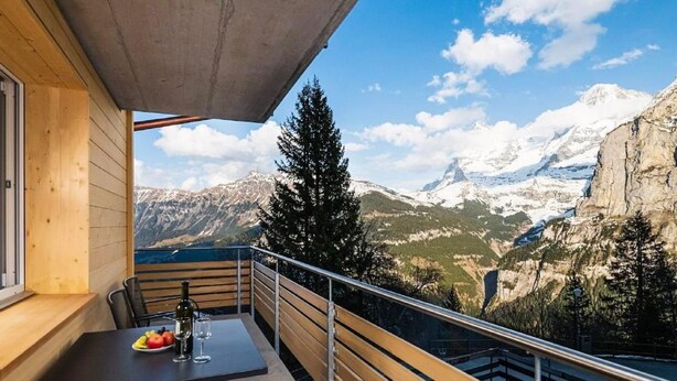 A balcony with a table set for two, overlooking a mountainous landscape with snow-capped peaks. - Chalet Raufthubel by Interhome (Lauterbrunnen)