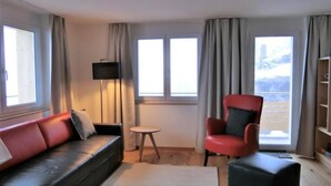 A living room with a red sofa, a red armchair, a small round table, and a television on a stand. - Chalet Raufthubel by Interhome (Lauterbrunnen)
