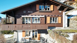 Una cabaña con fachada de madera, ventanas grandes y un balcón con mobiliario exterior.