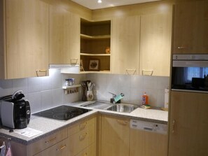 Een moderne keuken met houten kastjes, een inbouwoven, een vaatwasser en een koffiezetapparaat.