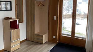 Una habitación con un armario de madera, una pequeña estantería y un ventanal corredero que da a un espacio exterior cubierto.