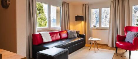 Una sala moderna con un sofá de cuero negro, un sillón rojo, una mesa de centro de madera y una mesita auxiliar.