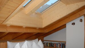 Een slaapkamer met dakraam, een bed met kussens, een nachtkastje en een plank met boeken.