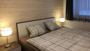 A hotel room with a wooden headboard, two bedside lamps, a bed with a plaid duvet, and a window with dark curtains. - Chäs-Gruebi Wohnung Hirsch by Interhome (Lauterbrunnen)