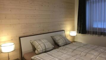 Une chambre d’hôtel avec une tête de lit en bois, deux lampes de chevet, un lit recouvert d’une couette à carreaux et une fenêtre avec des rideaux foncés.