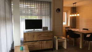 A compact living space with a TV on a wooden cabinet, a dining table with chairs, and a small side table. - Chäs-Gruebi Wohnung Hirsch by Interhome (Lauterbrunnen)