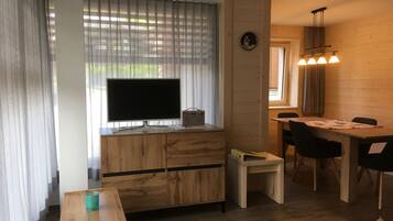 Un espace de vie compact comprenant un téléviseur posé sur un meuble en bois, une table à manger avec des chaises et une petite table d’appoint.