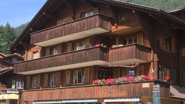 A traditional wooden building with a balcony adorned with colorful flowers, a sign indicating a restaurant, and a green trash bin outside. - Chäs-Gruebi Wohnung Hirsch by Interhome (Lauterbrunnen)