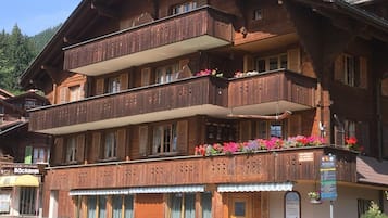 Un bâtiment traditionnel en bois, doté d’un balcon orné de fleurs colorées, d’une enseigne indiquant un restaurant et d’une poubelle verte à l’extérieur.