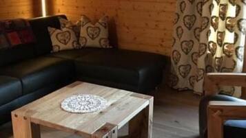 L’intérieur d’un chalet chaleureux, avec un plafond en bois, un canapé noir, une table basse en bois et un rideau à motifs.