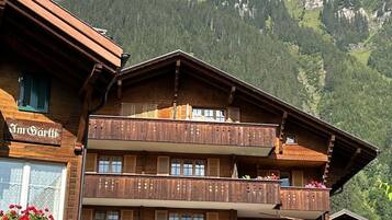 Un immeuble en bois à plusieurs étages, doté de balcons, entouré d’une végétation luxuriante et de montagnes.