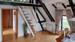 Ruime kamer met een houten trap, een eetgedeelte met een tafel gedekt voor twee personen, en uitzicht op de omgeving.