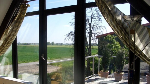 Een kamer met grote ramen, een radiator en uitzicht op een groen veld en een weg.