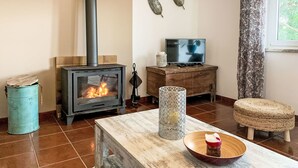 A living room with a wood-burning stove, a television, a table with a bowl, and a window with curtains. - Charmantes Ferienhaus mit schöner Aussicht, 2 Sc by Interhome (Aljezur)