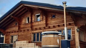 Eine Holzhütte mit großem Fassofen, Holzfenstern und einem mit Schnee bedeckten Dach.