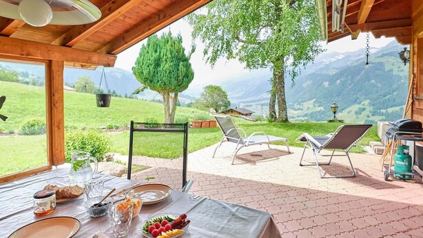 Ein Essbereich mit Tisch für zwei Personen, Gartenstühlen, einem Grill und Blick auf die Berge.