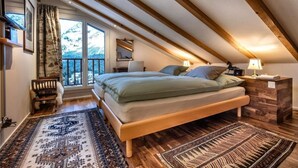 A bedroom with a large bed, wooden beams, a view of mountains, and a balcony. - Luxus Alpenchalet Brigitta I by Interhome (Arosa)