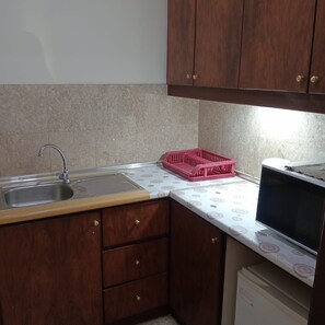 A compact kitchen with a sink, wooden cabinets, a microwave, and a pink dish rack. - Homestay Suite At Times Square KL (Kuala Lumpur)