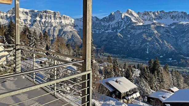 A mountain view from a wooden balcony with metal railings, overlooking snow-covered buildings and rugged mountains. - Flumserberg by Interhome (Flumserberg Tannenheim)