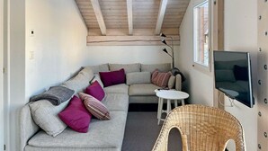 A cozy living room with a high ceiling, a sectional sofa, a small round table, a wicker chair, and a TV mounted on the wall. - Flumserberg by Interhome (Flumserberg Tannenheim)