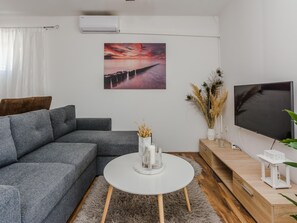 Ein modernes Wohnzimmer mit einem grauen Sofa, einem weißen Couchtisch, einem Fernseher und einem Gemälde, das einen Sonnenuntergang zeigt.