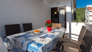Ein überdachter Essbereich im Freien mit einem Tisch für zwei Personen, ausgestattet mit einer blau-weißen Tischdecke und einer Schüssel mit Orangen.