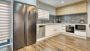 A modern kitchen with a stainless steel refrigerator, built-in oven, microwave, and wooden cabinets. - Boutique Hillside Heaven near AKLD Airport (Papatoetoe Auckland)