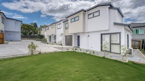 A row of modern, single-story houses with a well-maintained lawn and a clear sky. - Boutique Hillside Heaven near AKLD Airport (Papatoetoe Auckland)