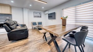 A modern living room with a wooden dining table, black leather sofa, and two armchairs. - Boutique Hillside Heaven near AKLD Airport (Papatoetoe Auckland)
