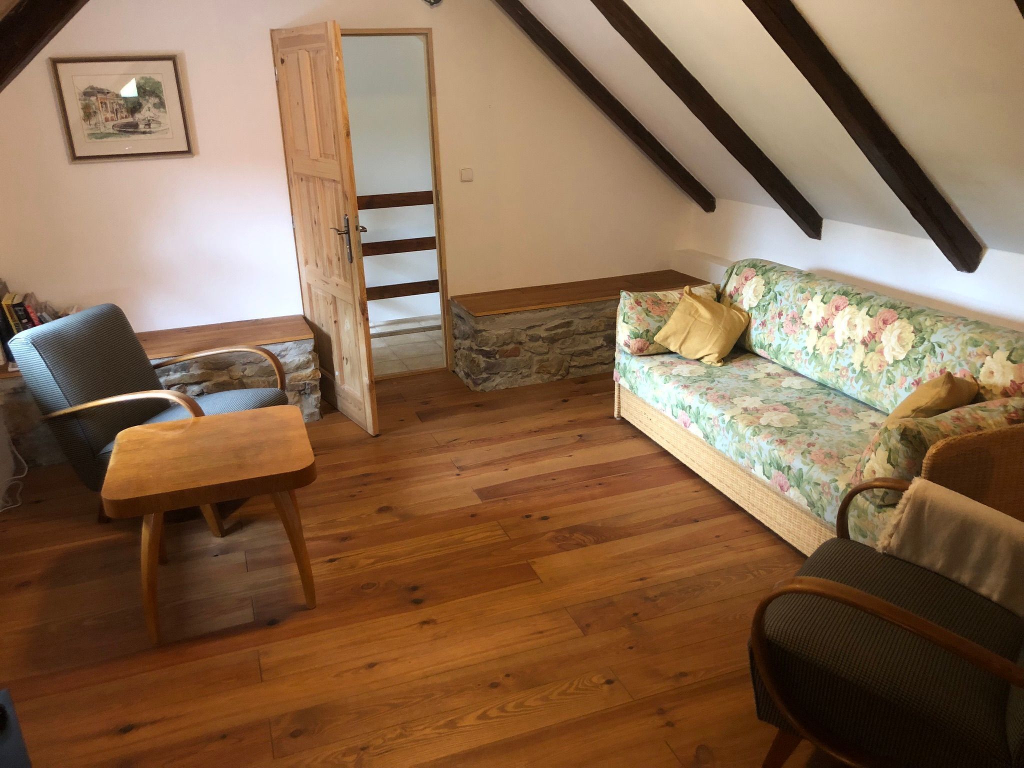 Ein gemütliches Schlafzimmer im Loft-Stil mit Holzboden, einem floralen Sofa, einem Sessel und einer Holzbank.