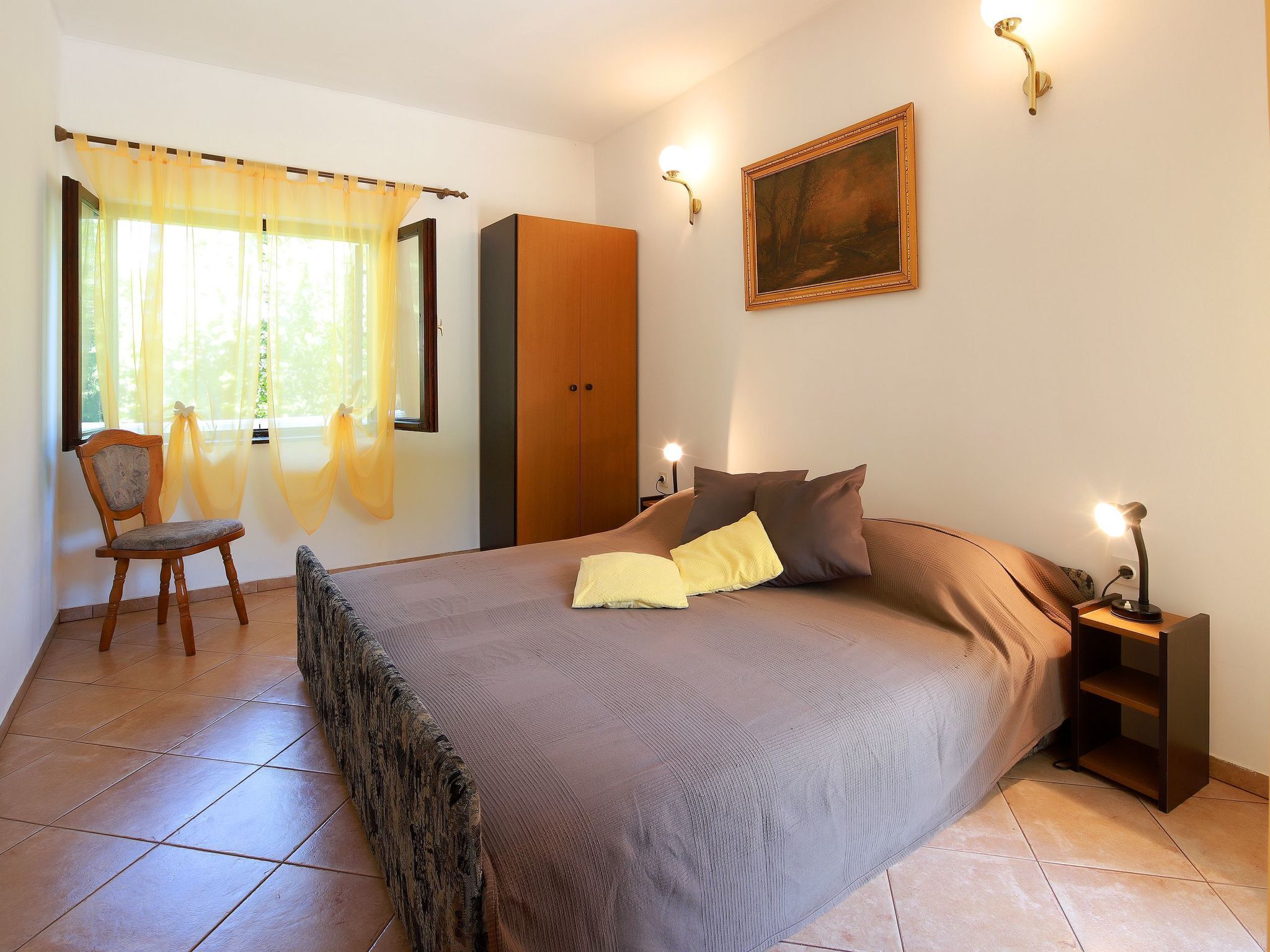 Une chambre à coucher avec un lit, une chaise, une armoire et un tableau accroché au mur.