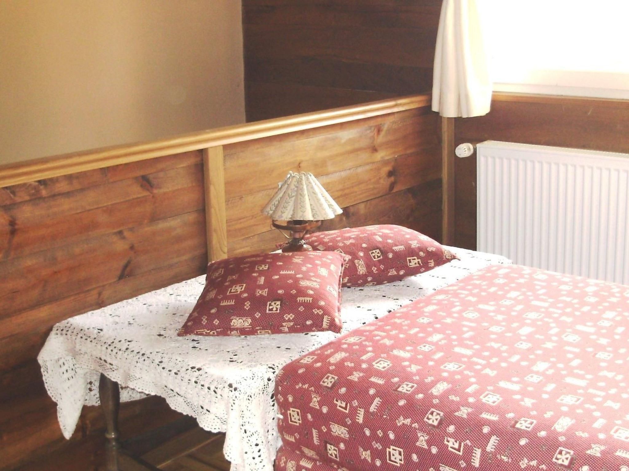 A bedroom with a wooden headboard, a white lace tablecloth, and two red pillows with a pattern.