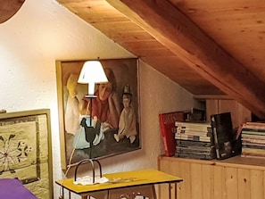 Une pièce avec un plafond en bois, un tableau, une petite table avec une lampe et une pile de livres.