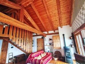 A wooden interior with a staircase, a sofa, a radiator, and a wood-burning stove.
