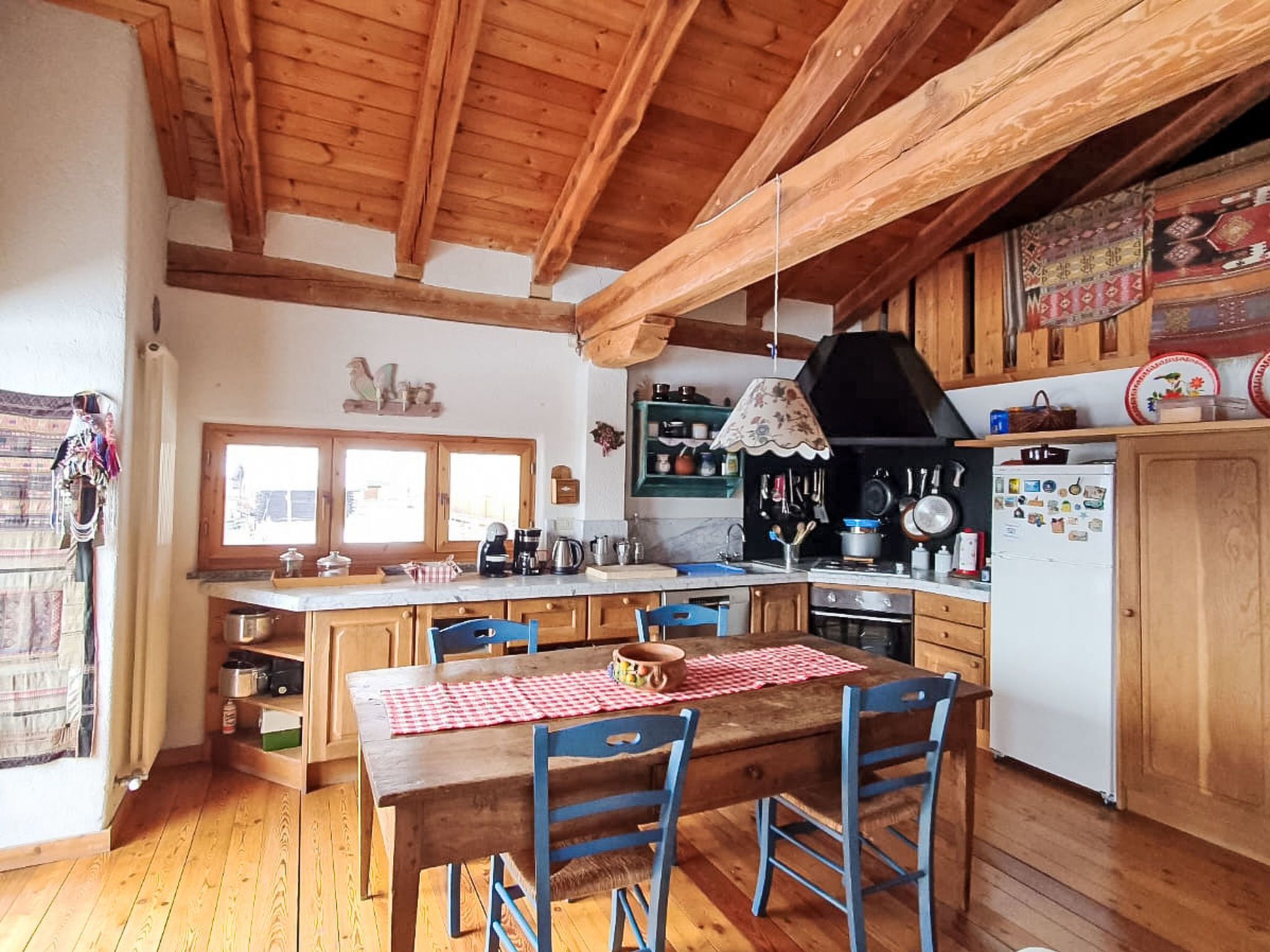 A kitchen with wooden beams, a dining table with chairs, a stove, and a refrigerator.