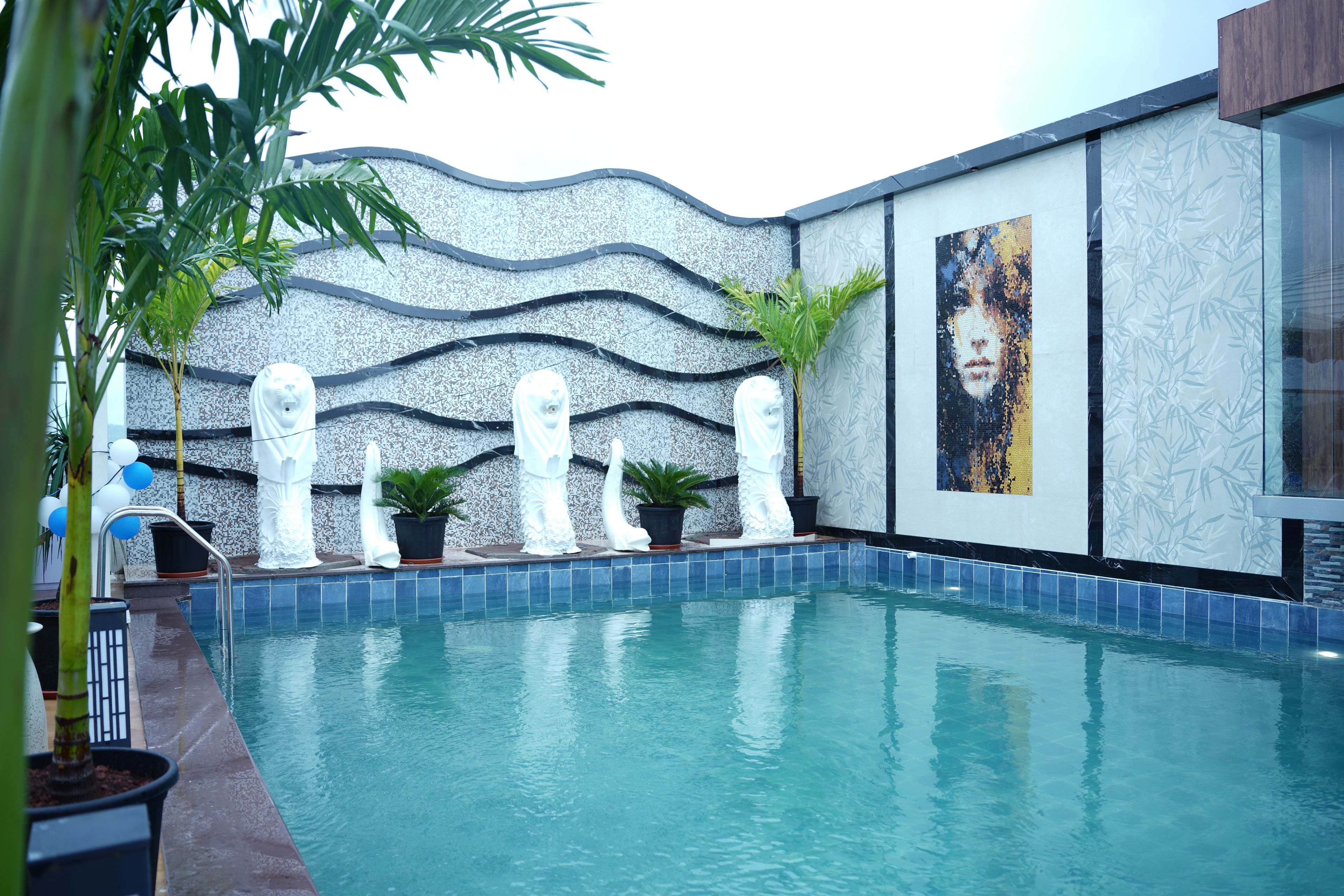 Piscina com borda azulejada, rodeada por plantas em vasos e estátuas brancas.