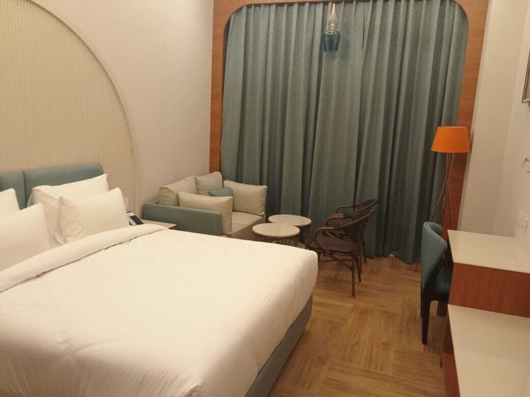 A hotel room with a large bed, a small sofa, two chairs, a round table, and a curtain.